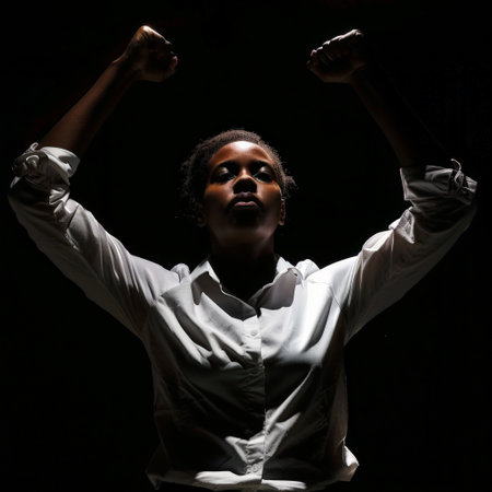 A determined female performer stands tall with raised fists, embodying strength and resilience in a dark theater setting. The contrast highlights her powerful expression.の素材