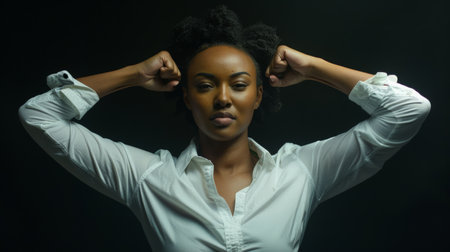A woman stands confidently with her arms raised, displaying strength and empowerment. She is dressed in a button-up shirt, exuding a powerful presence against a dark background.の素材