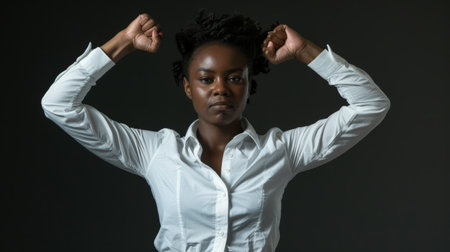 A woman stands with her fists raised, exuding confidence and empowerment. She wears a white blouse, set against a dark background, embodying strength and resilience.の素材