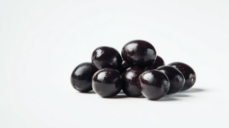 A cluster of ripe black olives rests on a bright white surface, highlighting their shine.の写真素材