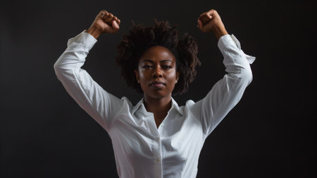 A confident woman stands with her arms raised, expressing strength and determination. The dark background emphasizes her powerful presence during a moment of empowerment.の素材