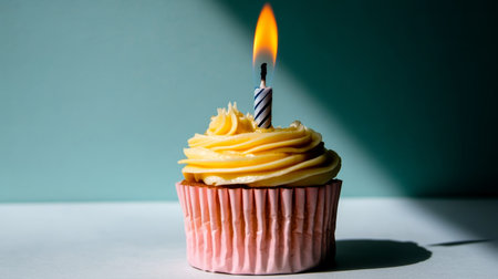 A vibrant yellow birthday cupcake sits proudly with a lit candle atop, casting a warm glow in a charming atmosphere. Perfect for celebrating moments.の素材