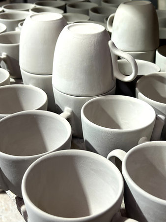 Ceramic cups and mugs crafted from clay are neatly arranged in a pottery studio, showing them...