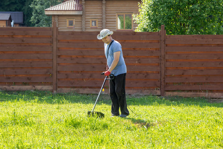 man mows the grass with a string trimmer