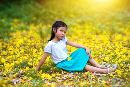 Cute little girl sitting on the ground beside a large bouquet of bright yellow flowers.The girl look at cameraの写真素材