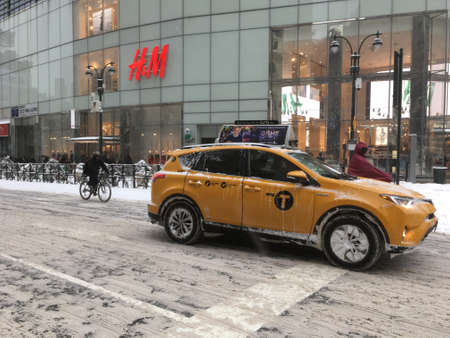 4 January 2018 - New York City: Yellow cab and two bike riders in front of H&M in midtown Manhattan on a snowy day in New York City.のeditorial素材