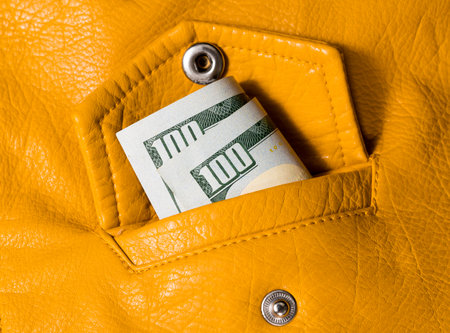 Close up of one hundred dollar bill in the pocket of a yellow leather jacket