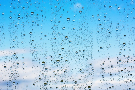 Water droplets on glass against the blue sky with cloudsの写真素材