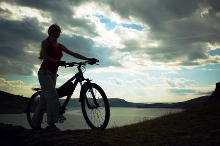 Silhouette of the girl with a bicycle against mountainsの写真素材
