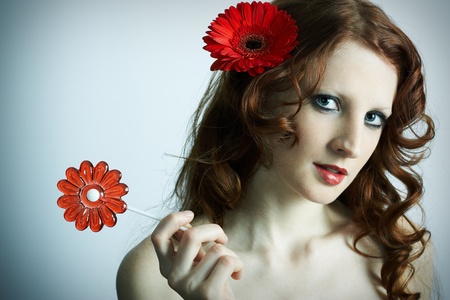 The beautiful young girl with a red flower and caramelの写真素材