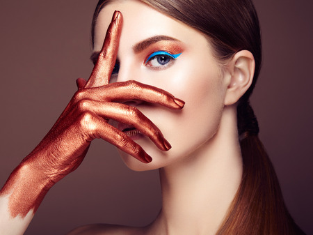 Portrait of beautiful young woman with art make-up. Bronze hand. Beauty fashionの写真素材