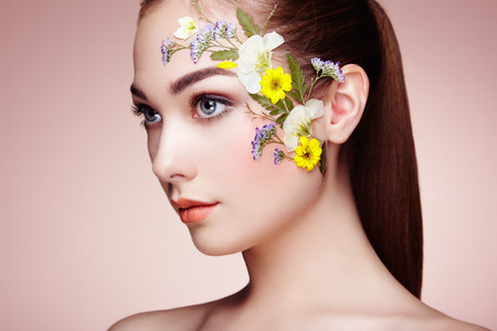 Face of beautiful woman decorated with flowers. Perfect makeup. Beauty fashion. Eyelashes. Cosmetic Eyeshadowの写真素材