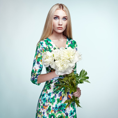 Fashion portrait of elegant woman with summer flowers. Blonde girl. Perfect make-up. Hairstyle. Summer dress. Peoniesの写真素材