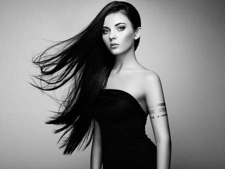 Fashion portrait of elegant woman with magnificent hair. Brunette girl. Perfect make-up. Girl in elegant dress. Flash tattoo gold. Black and whiteの写真素材