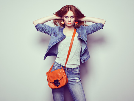 Fashion portrait of beautiful young woman with red hair. Girl in blouse and jeans. Jewelry and hairstyle. Girl with handbagの写真素材