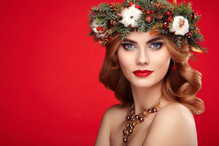 Portrait of beautiful young woman with Christmas wreath. Beautiful New Year and Christmas tree holiday hairstyle and makeup. Beauty girl portrait isolated on white background. Colorful makeup and hairの写真素材