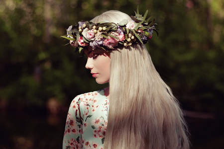 Beautiful blonde woman with flower wreath on her head. Beauty girl with flowers hairstyle. Girl in a summer forest. Fashion photoの写真素材