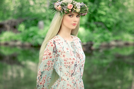 Beautiful blonde woman with flower wreath on her head. Beauty girl with flowers hairstyle. Girl in a summer forest. Fashion photoの写真素材