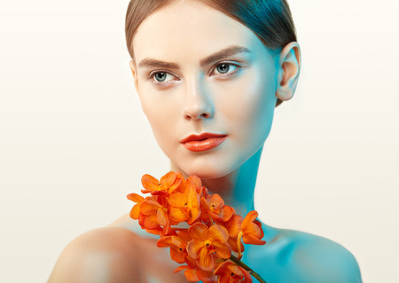 Portrait of beautiful young woman with orchid. Brunette woman with luxury makeup. Perfect skin. Eyelashes. Cosmetic eyeshadow. Orange flowersの写真素材