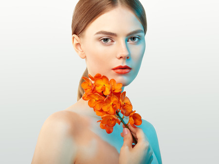 Portrait of beautiful young woman with orchid. Brunette woman with luxury makeup. Perfect skin. Eyelashes. Cosmetic eyeshadow. Orange flowersの写真素材