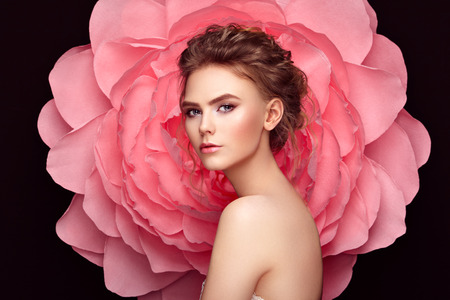Beautiful woman on the background of a large flower. Beauty summer model girl with pink peony. Young woman with elegant hairstyle and makeup. Fashion photoの写真素材