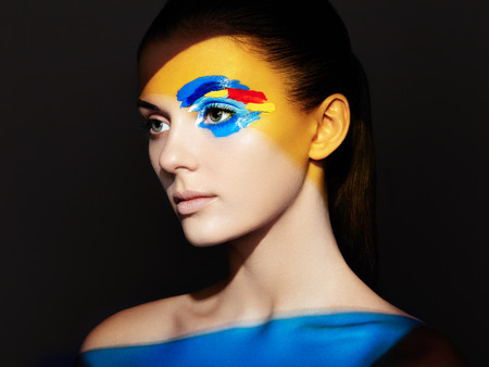 Fashion model woman with colored face painted. Beauty fashion art portrait of beautiful woman with colorful abstract makeup. Face painted paints. Multicolor designの写真素材