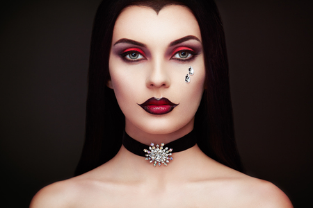 Halloween Vampire Woman portrait. Beautiful Glamour Fashion Sexy Vampire Lady with long dark Hair, beauty make up and Costumeの写真素材