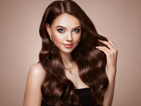 Brunette Girl with Long Healthy and Shiny Curly Hair. Care and Beauty. Beautiful Model Woman with Wavy Hairstyle. Make-Up and Jewelryの写真素材