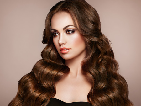 Brunette Girl with Long Healthy and Shiny Curly Hair. Care and Beauty. Beautiful Model Woman with Wavy Hairstyle. Make-Up and Black Dressの写真素材