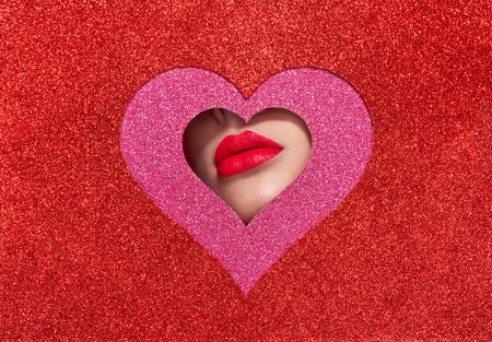 Beautiful Plump Bright Lips Of a Young Beautiful Woman with Red Lipstick Look Into the Pattern of Heart Shaped made of Colored Paper. Holiday Patterns. Valentine's Day. Beautiful Love Make-upの写真素材
