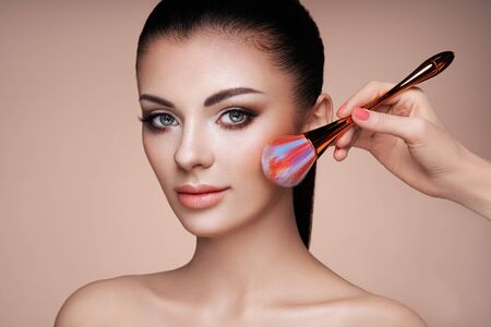 Beautiful Woman applies Skin Tone with Brush. Beautiful Woman face. Perfect Makeup. Skincare Foundation. Brushes Makeup Artistの写真素材