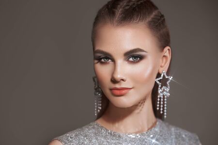 Portrait beautiful woman with jewelry. Brunette girl with long smooth hair. Beauty fashion. Eyelashes. Cosmetic eyeshadow. Care and beauty hair products. Model in a silver dressの写真素材