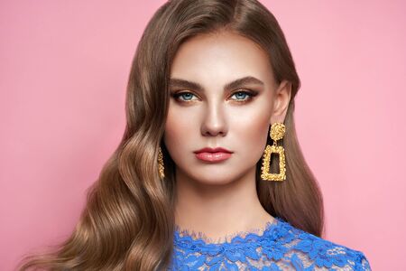 Brunette girl with perfect makeup. Beautiful model woman with curly hairstyle. Care and beauty hair products. Lady with fashionable gold makeup. Model with jewelry on pink backgroundの写真素材