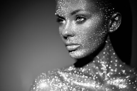 Fashion model woman in bright sparkles and lights posing in studio. Portrait of beautiful sexy woman. Art design glitter glowing make up. Black and white photographyの写真素材