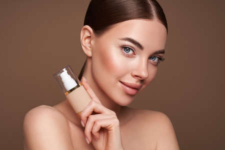 Portrait beautiful young woman with clean fresh skin. Model with foundation makeup bottle. Cosmetology, beauty and spaの写真素材