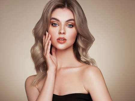 A beautiful young woman with shiny wavy blonde hair. Model with healthy skin, close up portrait. Cosmetology, beauty and spaの写真素材