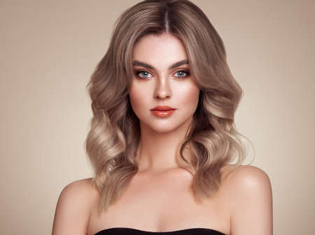 A beautiful young woman with shiny wavy blonde hair. Model with healthy skin, close up portrait. Cosmetology, beauty and spaの写真素材