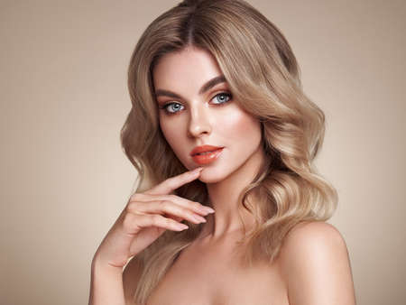 A beautiful young woman with shiny wavy blonde hair. Model with healthy skin, close up portrait. Cosmetology, beauty and spaの写真素材