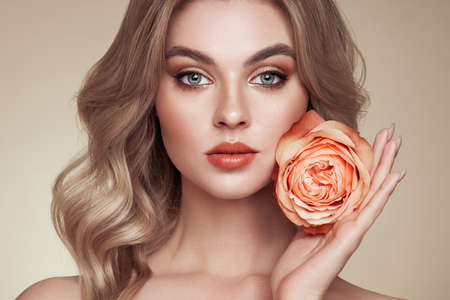 A beautiful young woman with shiny wavy blonde hair. Model with healthy skin, close up portrait. Girl with a rose flowerの写真素材