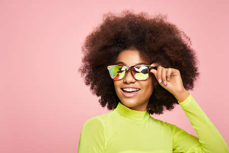 Beauty portrait of African American girl in colored holographic sunglasses. Beautiful black woman on pink background. Cosmetics, makeup and fashionの写真素材