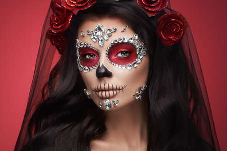 Portrait of a woman with sugar skull makeup over red background. Halloween costume and make-up. Portrait of Calavera Catrinaの写真素材
