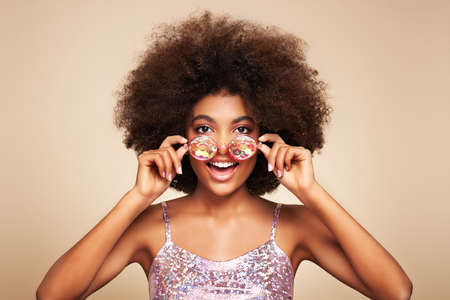 Beauty portrait of African  girl in holographic sunglasses. Beautiful black woman on beige background. Cosmetics, makeup and fashionの写真素材