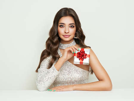 Beautiful woman in cocktail dress with gift box in hands. Beauty model with long curly hair. Christmas or New Year festivities. Holiday and Partyの写真素材