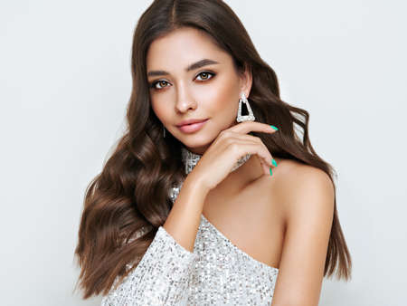Beautiful woman in cocktail dress posing on white background. Beauty model with long curly hair. Christmas or New Year festivities. Jewelry and manicureの写真素材