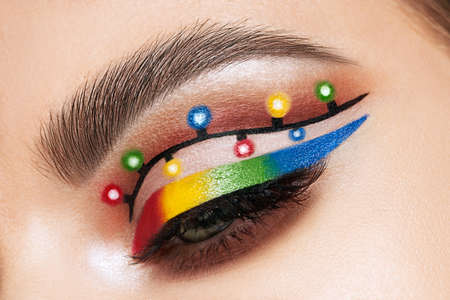 Eye of a girl with makeup Christmas lights. Winter christmas makeup. Beauty fashion. Eyelashes. Creative New Year's holiday makeup close-upの写真素材