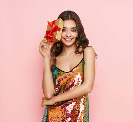 Beautiful woman in cocktail dress with gift box in hands. Beauty model with long curly hair. Christmas or New Year festivities. Holiday and Partyの写真素材