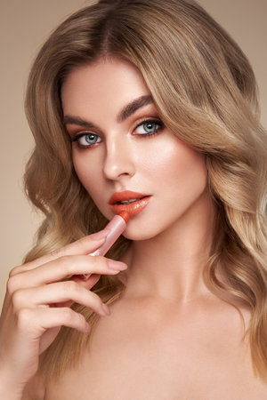 A beautiful young blonde woman applying lipstick. Model with healthy skin, close up portrait. Cosmetology, beauty and spaの写真素材