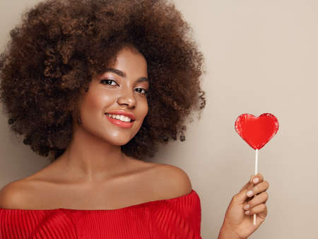 Beautiful portrait of an African girl with a heart shaped lollipop. Valentine's Day. Symbol of loveの写真素材