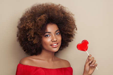 Beautiful portrait of an African girl with a heart shaped lollipop. Valentine's Day. Symbol of loveの写真素材