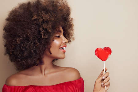 Beautiful portrait of an African girl with a heart shaped lollipop. Valentine's Day. Symbol of loveの写真素材